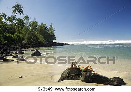 Stock Photo - Hawaii, Kauai, Ke'e Beach, Attractive Young Woman Laying On The Rocks.. Fotosearch