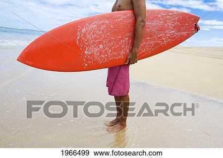 Stock Photo - Hawaii, Kauai, Man Holding Surfboard On Beach, View From Side.. Fotosearch