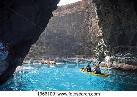 Stock Photo - Hawaii, Kauai, Na Pali Coast, Kayakers Exploring Sea Cave Along Coastline, Waterfall From Cliffside. Editorial Use Only.. Fotosearch