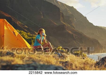 Hawaii, Kauai, Na Pali Coast, View of the Kalalau Mountains, Female camper sipping her drink at campsite. View Large Photo Image Stock Image - Hawaii, Kauai, Na Pali Coast, View of the Kalalau Mountains, Female camper sipping her drink at campsite.. Fotosearch