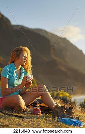 Stock Image - Hawaii, Kauai, Na Pali Coast, View of the Kalalau Mountains, Female camper enjoying the view from her campsite.. Fotosearch
