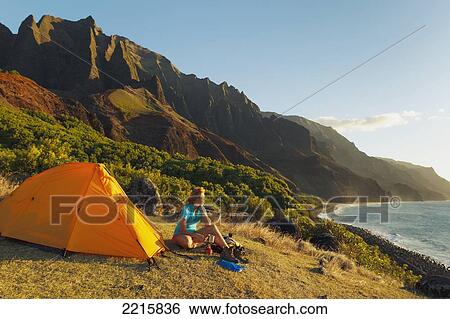 Stock Photograph - Hawaii, Kauai, Na Pali Coast, View of the Kalalau Mountains and ocean, Female camper enjoys the scenery.. Fotosearch