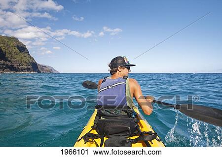 Stock Image - Hawaii, Kauai, Na Pali Coast, Young Man Kayaking Along Coastline. Editorial Use Only.. Fotosearch