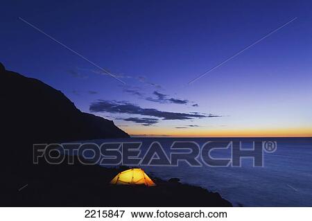 Stock Photo - Hawaii, Kauai, Na Pali Coastline and Kalalau Mountains, Iluminated tent at dusk.. Fotosearch