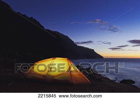 Stock Photography - Hawaii, Kauai, Na Pali Coastline and Kalalau Mountains, Ilumminated tent at dusk.. Fotosearch