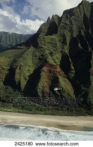 Stock Image - Hawaii, Kauai, Napali Coast, Helicopter flies along cliffs. Fotosearch