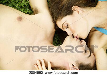 Stock Image - Hawaii, Kauai, North Shore, Couple Lay In Grass And Kiss.. Fotosearch