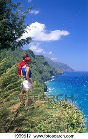 Stock Photo - Hawaii, Kauai, North Shore, Na Pali Coast Trail, Couple Hiking Take In Coastline View Side Angle. Fotosearch
