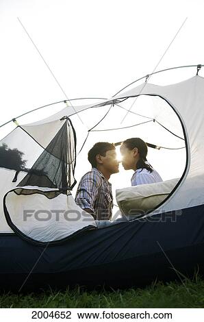 Stock Image - Hawaii, Kauai, North Shore, /Ncouple Lean In For Kiss In Tent.. Fotosearch