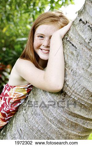 Stock Image - Hawaii, Kauai, North Shore, Young Girl With Red Hair And Freckles Leans Against A Palm Tree.. Fotosearch