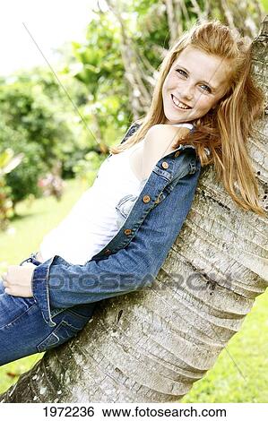 Stock Photograph - Hawaii, Kauai, North Shore, Young Woman With Red Hair And Freckles Leans On A Palm Tree Outside.. Fotosearch