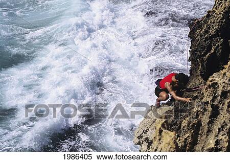 Stock Photography - Hawaii, Kauai, Poipu, Rock Climber On Cliff Overhang, Waves Crashing Below, View From Above.. Fotosearch