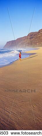 Stock Image - Hawaii, Kauai, Polihale Beach, Woman Walks Along Shore, Waves Roll In, Misty. Fotosearch