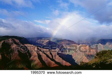 Stock Image - Hawaii, Kauai, Rainbow Over Waimea Canyon With Blue Skies, Afternoon Shadows. Fotosearch