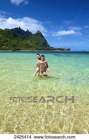 Picture - Hawaii, Kauai, Tunnels Beach, a young man holding a beautiful girl in the water.. Fotosearch