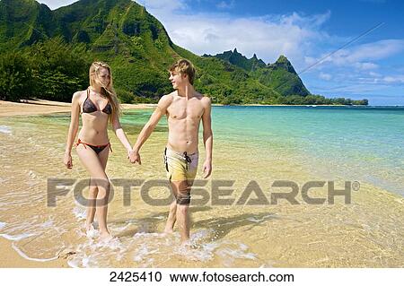 Stock Image - Hawaii, Kauai, Tunnels Beach, a young man and a beautiful girl walking on the shore.. Fotosearch