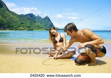 Hawaii, Kauai, Tunnels Beach, a young man and woman sitting in the sand, drawing a heart. View Large Photo Image Stock Image - Hawaii, Kauai, Tunnels Beach, a young man and woman sitting in the sand, drawing a heart.. Fotosearch