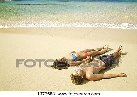 Stock Image - Hawaii, Kauai, Tunnels Beach, Beautiful Couple Laying On The Beach.. Fotosearch