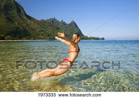 Stock Image - Hawaii, Kauai, Tunnel's Beach, Woman Leaps Into The Ocean.. Fotosearch