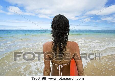 Stock Photo - Hawaii, Kauai, Woman Holding Surfboard On Beach, View From Behind.. Fotosearch
