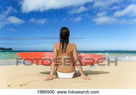 Stock Image - Hawaii, Kauai, Woman Sitting On Beach With Surfboard, View From Behind.. Fotosearch