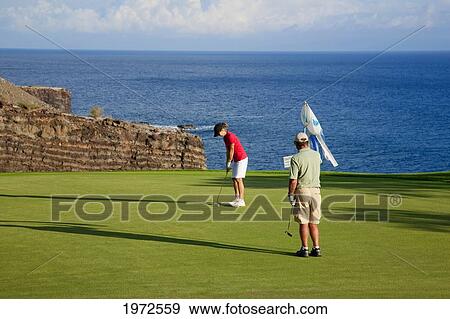 Stock Photo - Hawaii, Lanai, Couple Putting On The Green At The Challenge At Manele Golf Course.. Fotosearch