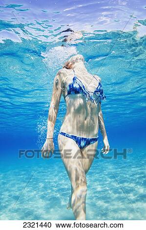 Stock Image - Hawaii, Lanai, Manele Bay, Young Woman Swimming Toward Ocean Surface.. Fotosearch