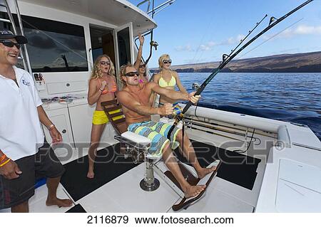 Stock Photo - Hawaii, Lanai, The crew and clients on a sportfishing charter boat reeling in a fish.. Fotosearch