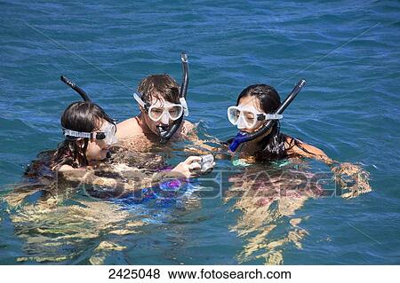 Stock Photo - Hawaii, Lanai, Three friends looking at pictures from their underwater camera.. Fotosearch
