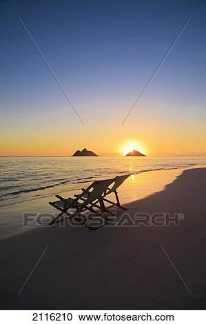 Stock Image - Hawaii, Lanikai, Pair of empty beach chairs at sunset.. Fotosearch