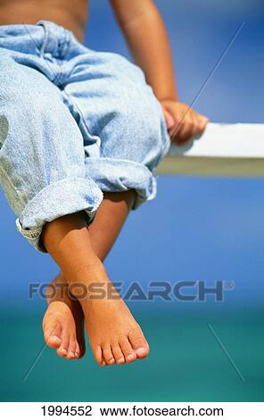 Stock Image - Hawaii, Legs And Feet Of Young Boy Sitting On A Bench By The Ocean. Fotosearch