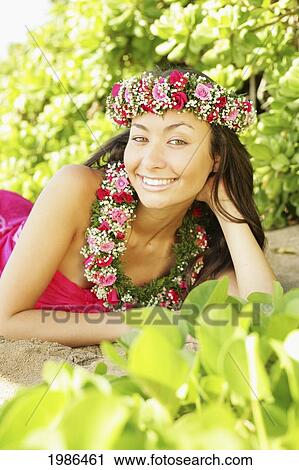 Stock Image - Hawaii, Local Girl Laying On Sand Wearing Flower Leis Surrounded By Bright Vegetation.. Fotosearch