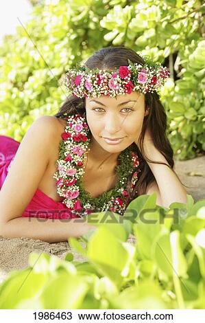 Stock Image - Hawaii, Local Girl Laying On Sand Wearing Flower Leis Surrounded By Bright Vegetation.. Fotosearch