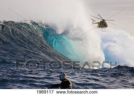 Stock Photo - Hawaii, Maui, A Helicopter Filming A Tow-In Surfer At Peahi (Jaws). The Head In The Foreground Is Driving A Jetski.. Fotosearch