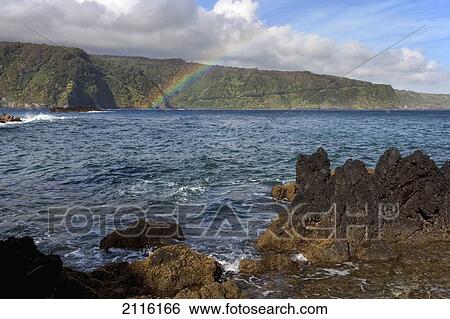 Stock Photograph - Hawaii, Maui, A rainbow forms over the road to Hana in Keanae.. Fotosearch