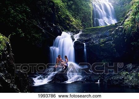 Hawaii, Maui, Couple Sit On Rock In Middle Of Waterfall. View Large Photo Image Stock Photograph - Hawaii, Maui, Couple Sit On Rock In Middle Of Waterfall.. Fotosearch