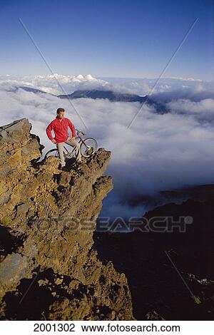 Stock Image - Hawaii, Maui, Haleakala, Man With Mountain Bike Along On Cliff Above Clouds Rest Enjoy Scenery. Fotosearch