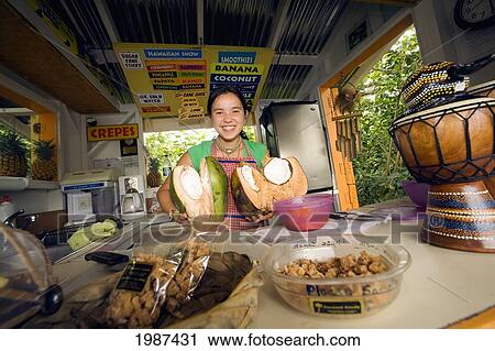 Stock Image - Hawaii, Maui, Hana, Fruit And Souvenir Stand At Huelo Lookout, Girl Holding Coconuts Behind The Counter.. Fotosearch