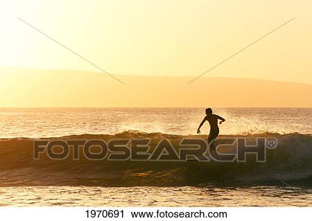 Stock Image - Hawaii, Maui, Lahina, Surfer Rides A Wave At Sunset. For Editorial Use Only.. Fotosearch