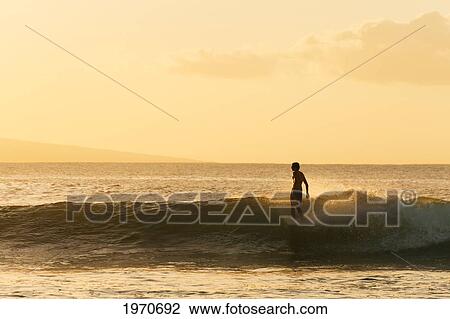 Stock Image - Hawaii, Maui, Lahina, Surfer Rides A Wave At Sunset. For Editorial Use Only.. Fotosearch