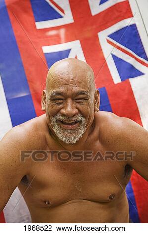 Stock Image - Hawaii, Maui, Local Hawaiian Man Sitting In Front Of A Hawaiian Flag (Soft Focus).. Fotosearch
