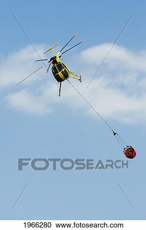 Stock Image - Hawaii, Maui, Ma'alaea, Fire Helicopter Carrying Water Bucket To Help Put Out Wildfire. Editorial Use Only.. Fotosearch