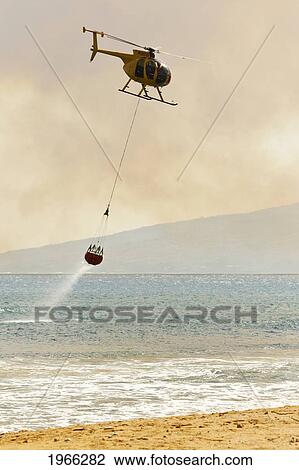 Stock Image - Hawaii, Maui, Ma'alaea, Fire Helicopter Collecting Ocean Water To Help Put Out Wildfire. Editorial Use Only.. Fotosearch