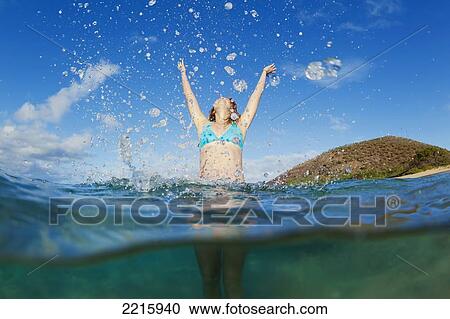 Stock Image - Hawaii, Maui, Makena Beach, A young woman plays in the ocean, Throws water in the air.. Fotosearch
