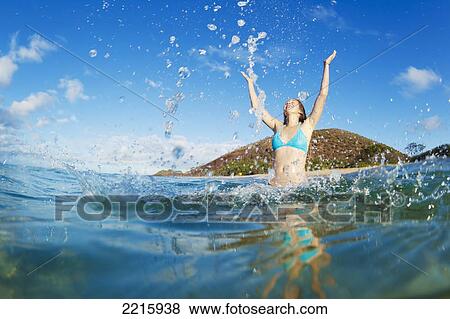 Stock Photo - Hawaii, Maui, Makena Beach, A young woman plays in the ocean, Throws water in the air.. Fotosearch