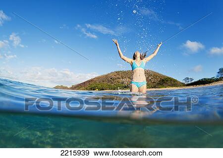 Stock Photo - Hawaii, Maui, Makena Beach, A young woman plays in the ocean, Throws water in the air.. Fotosearch