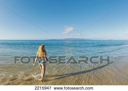 Stock Photo - Hawaii, Maui, Makena Beach, Young woman walks into ocean to cool off.. Fotosearch