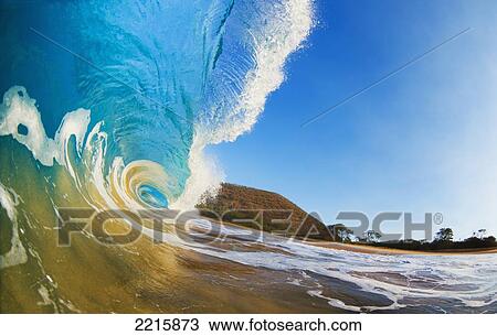 Stock Image - Hawaii, Maui, Makena, Beautiful blue ocean wave breaking at the beach.. Fotosearch