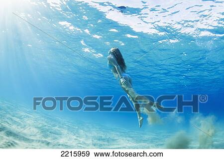 Stock Photo - Hawaii, Maui, Makena, Young woman swimming to ocean surface, Dropping sand as she goes.. Fotosearch