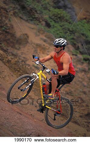Stock Image - Hawaii, Maui, Nakalele Point, Man Mountain Biking Uphill, Full Length Side View. Fotosearch